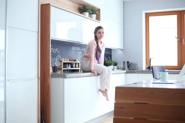 Jovem mulher sentada na mesa na cozinha . — Fotografia de Stock