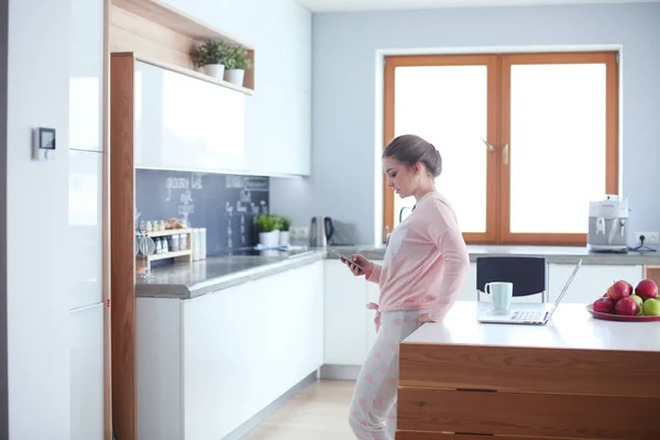 Vrouw met behulp van mobiele telefoon staande in de moderne keuken. — Stockfoto