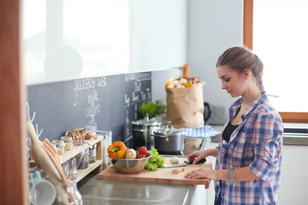 Junge Frau schneidet Gemüse in Küche neben Schreibtisch. — Stockfoto