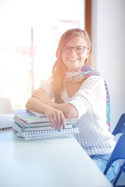 Jonge vrouw zit achter een bureau tussen de boeken. Studenten — Stockfoto