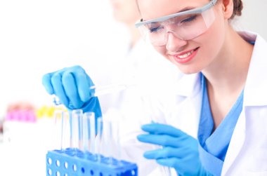 Kadın araştırmacı, beyaz arka planda izole edilmiş ilaç şişeleri ve mataralarla çevrili.