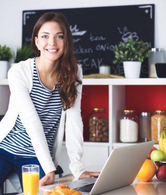 Dizüstü bilgisayar kullanarak ve mutfakta oturmuş çekici genç kadın