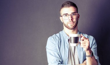 Yakışıklı bir genç adam ayakta ve bir fincan kahve onun elinde tutan portresi