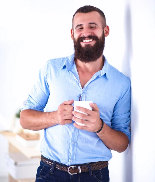 Jovem homem de pé perto da parede e segurando xícara de café — Fotografia de Stock