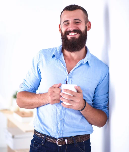 Joven parado cerca de la pared y sosteniendo una taza de café — Foto de Stock