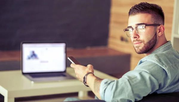 Jonge man met telefoon en werkt op de laptop — Stockfoto