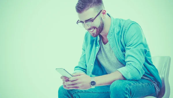 Junger Mann sitzt auf Stuhl und benutzt Handy — Stockfoto