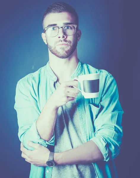 Portret przystojny, młody człowiek, stojąc i trzymając kubek kawy w rękach — Zdjęcie stockowe