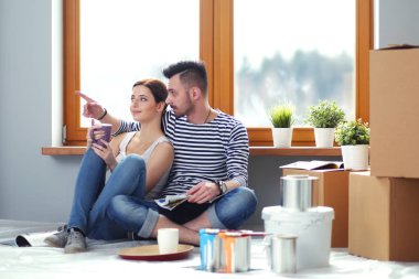 Yeni evin içini boyayan mutlu, gülümseyen genç bir çift portresi. Genç çift