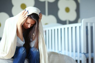 Genç çocuk karyolası yakın yatağın üstüne oturan kadın yorgun. Genç anne.