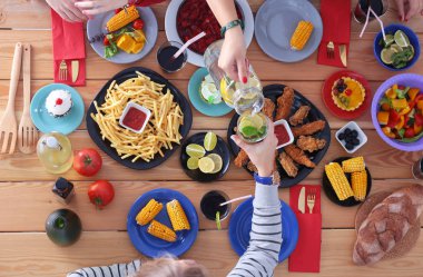 Ahşap masada otururken birlikte yemek yiyen bir grup insanın üst düzey görüntüsü. Masada yemek var. İnsanlar fast food yiyor..