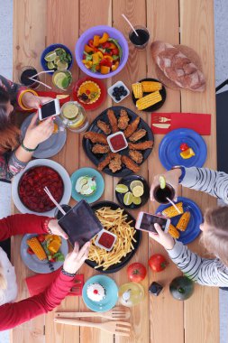 Ahşap masada otururken birlikte yemek yiyen bir grup insanın üst düzey görüntüsü. Masada yemek var. İnsanlar fast food yiyor..