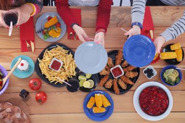 Ahşap masada otururken birlikte yemek yiyen bir grup insanın üst düzey görüntüsü. Masada yemek var. İnsanlar fast food yiyor..