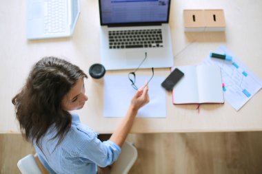 Ofis masasında oturan genç bir kadın dizüstü bilgisayar ekranına bakıyor. Genç kadın.