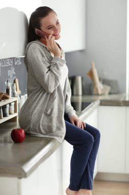 modern mutfakta otururken cep telefonu kullanan kadın.