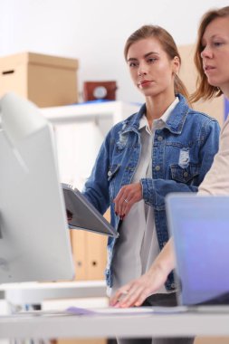 Masanın yanında duran iki genç kadın enstrüman, plan ve dizüstü bilgisayarla.