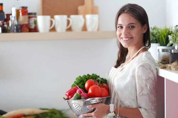 Jeune femme souriante tenant des légumes debout dans la cuisine. Jeune femme souriante — Photo