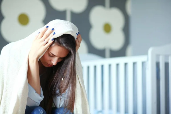 Ung trött kvinna som sitter på sängen nära barnens spjälsäng. Ung mamma. — Stockfoto