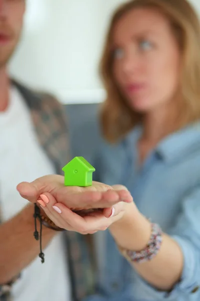 Casa modello in mano a una coppia, in piedi in una nuova casa. Modello di casa . — Foto Stock