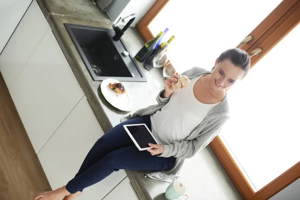 Hermosa joven usando una tableta digital en la cocina. — Foto de Stock