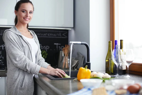 Hermosa joven lavando verduras para ensalada mientras está de pie en la cocina . —  Fotos de Stock