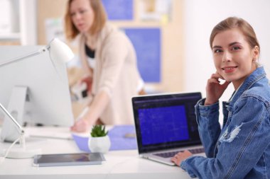 İki genç kadın masada enstrümanlar, planlar ve dizüstü bilgisayarlarla oturuyor..