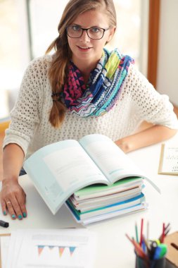 Kitapların arasında bir masada oturan genç bir kadın. Öğrenci