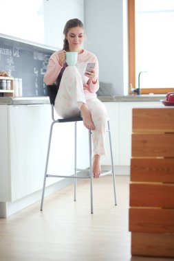 modern mutfakta otururken cep telefonu kullanan kadın.