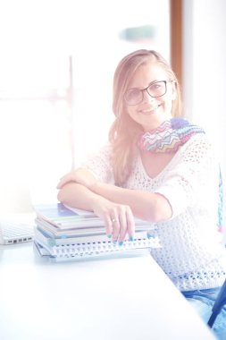 Kitapların arasında bir masada oturan genç bir kadın. Öğrenci