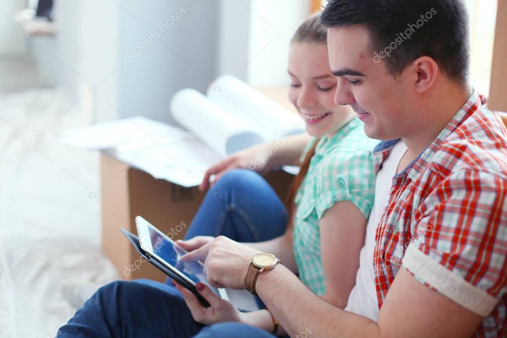 Couple moving in house sitting on the floor with ipad. Couple
