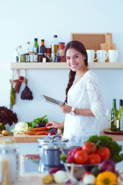 Mutfağında yemek için bir tablet bilgisayar kullanan genç kadın. Genç kadın