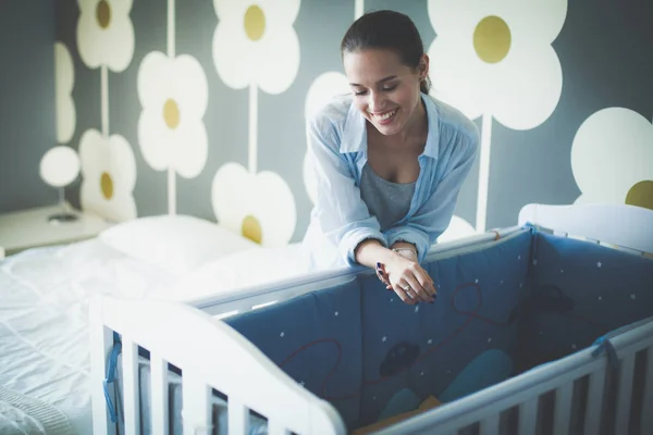 Jonge vrouw stond in de buurt van childrens kinderbed. Jonge moeder — Stockfoto