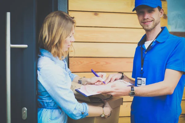 Repartidor sonriente con uniforme azul que entrega la caja de paquetes al destinatario: concepto de servicio de mensajería. Repartidor sonriente en uniforme azul — Foto de Stock