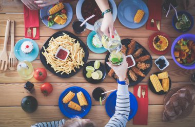 Ahşap masada otururken birlikte yemek yiyen bir grup insanın üst düzey görüntüsü. Masada yemek var. İnsanlar fast food yiyor..
