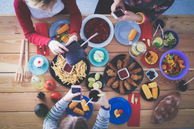 Ahşap masada otururken birlikte yemek yiyen bir grup insanın üst düzey görüntüsü. Masada yemek var. İnsanlar fast food yiyor..