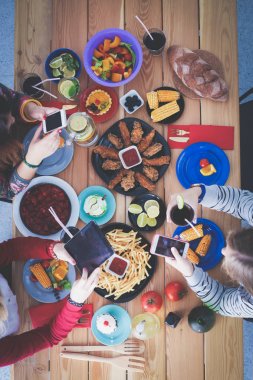 Ahşap masada otururken birlikte yemek yiyen bir grup insanın üst düzey görüntüsü. Masada yemek var. İnsanlar fast food yiyor..