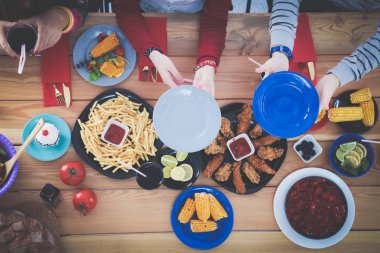 Ahşap masada otururken birlikte yemek yiyen bir grup insanın üst düzey görüntüsü. Masada yemek var. İnsanlar fast food yiyor..