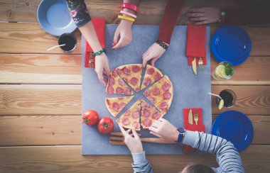 Ahşap masada otururken birlikte yemek yiyen bir grup insanın üst düzey görüntüsü. Masada yemek var. İnsanlar fast food yiyor..