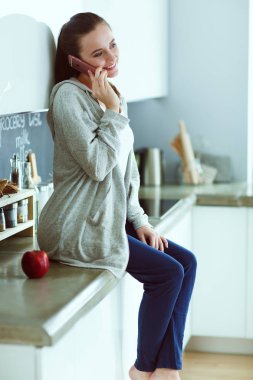 modern mutfakta otururken cep telefonu kullanan kadın.