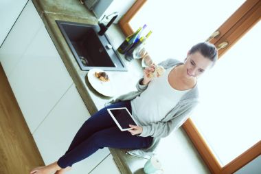 Mutfakta dijital tablet kullanan güzel genç bir kadın..