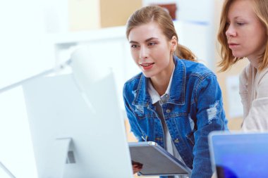 Masanın yanında duran iki genç kadın enstrüman, plan ve dizüstü bilgisayarla.