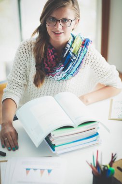 Kitapların arasında bir masada oturan genç bir kadın. Öğrenci