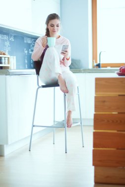 modern mutfakta otururken cep telefonu kullanan kadın.