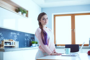 Cep telefonu ayakta modern mutfak kullanan kadın.