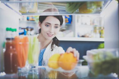 Sağlıklı yiyecek, sebze ve meyvelerle dolu açık buzdolabının yanında duran kadın portresi. Kadın portresi
