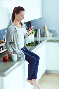 modern mutfakta otururken cep telefonu kullanan kadın.