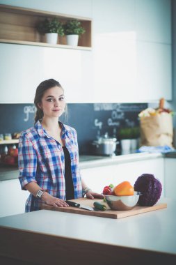 Masanın yanındaki mutfakta sebze doğrayan genç bir kadın..