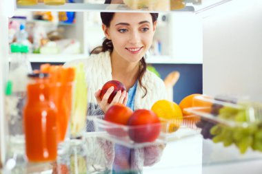 Sağlıklı yiyecek, sebze ve meyvelerle dolu açık buzdolabının yanında duran kadın portresi. Kadın portresi