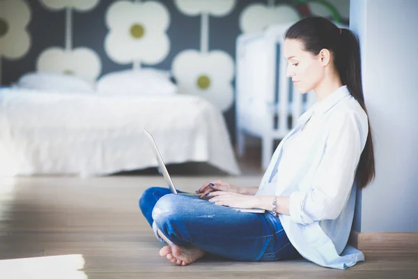 Jonge vrouw zittend op de vloer in de buurt van childrens kinderbed met laptop. Jonge moeder — Stockfoto