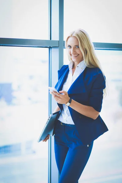 Businesswoman standing against office window talking on mobile phone . Businesswoman